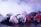 A variety of frozen berries including raspberries, blackberries, and blueberries are scattered on a surface. The berries are covered with a layer of frost, and mist surrounds them, creating a cold, wintry atmosphere.