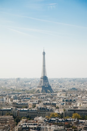 The Eiffel Tower stands prominently within a bustling cityscape, surrounded by an array of tightly packed buildings. The clear sky above adds a serene backdrop to the urban scene, creating a picturesque view of Paris.