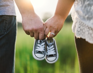 woman and man holding black crib shoes standing near green grass during daytime