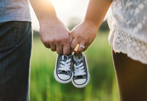 woman and man holding black crib shoes standing near green grass during daytime