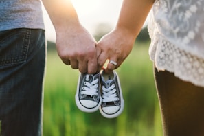 woman and man holding black crib shoes standing near green grass during daytime