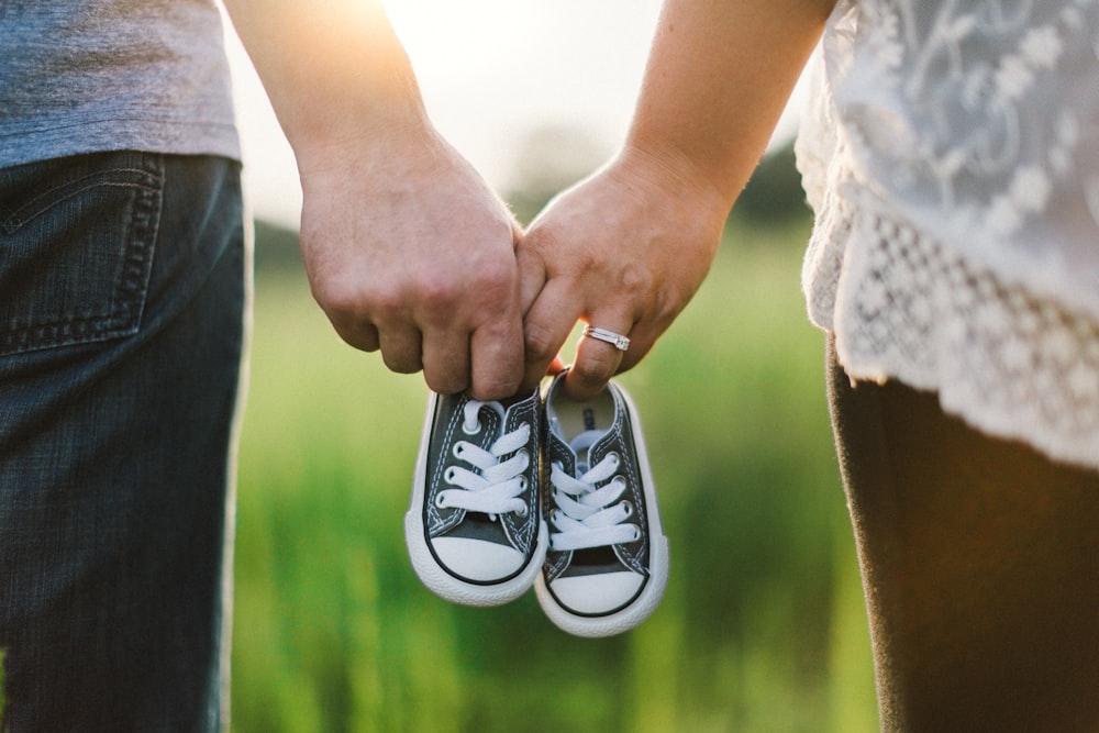 woman and man holding black crib shoes standing near green grass during daytime