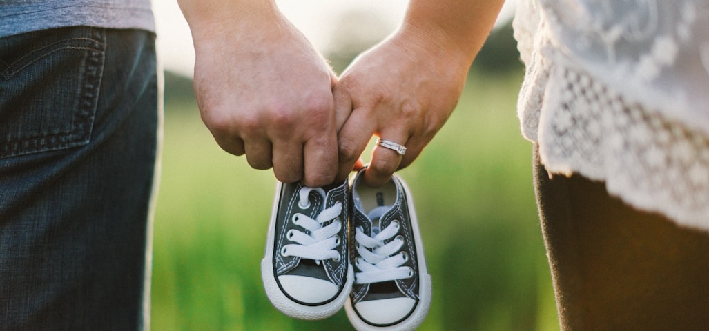 woman and man holding black crib shoes standing near green grass during daytime