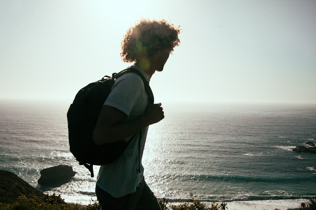 men wearing white-crew-neck t-shirt and black backpack watching the ocean,