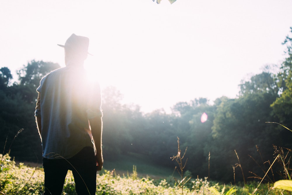 man standing on grass field with sun gazing