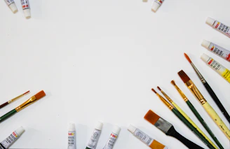 Minimalist arrangement of art supplies and a finished watercolor piece on a smooth cream surface.