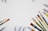 Various paintbrushes and tubes of artists' watercolor paints are scattered along the edges of a white surface, creating an arrangement that frames the central space.