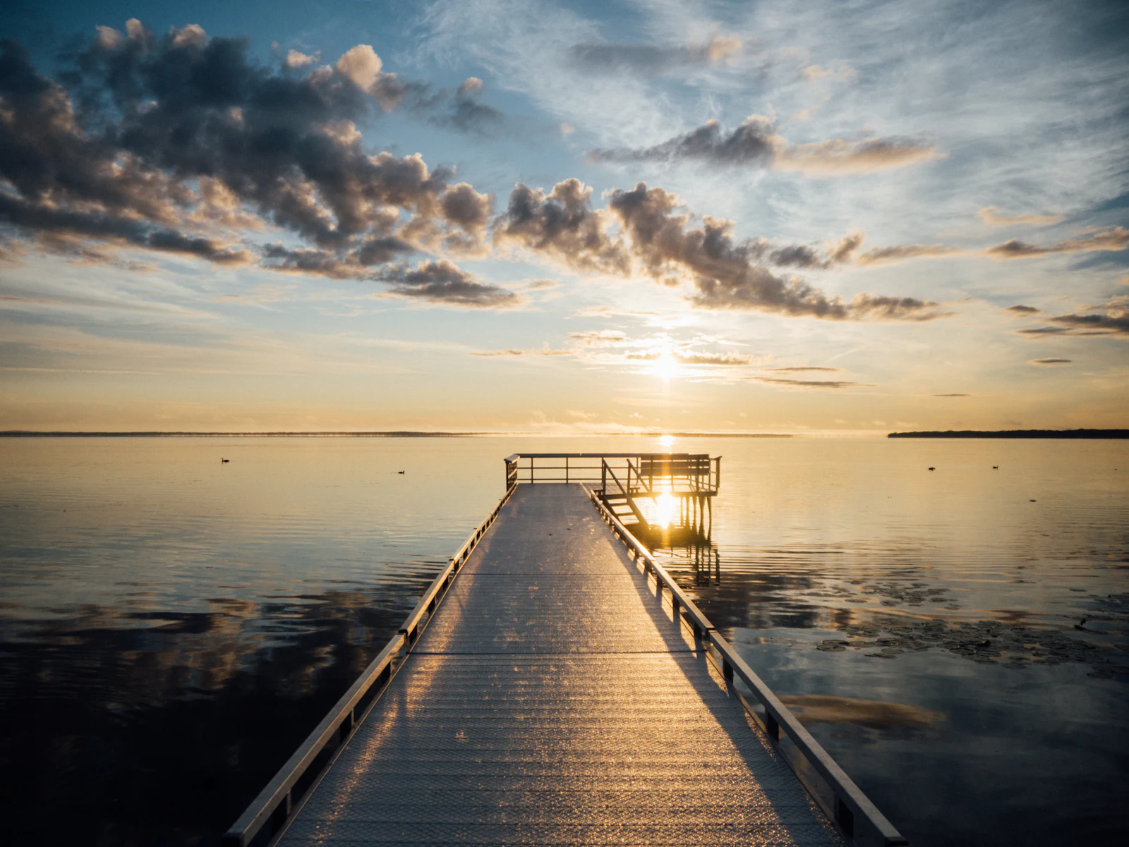 A wooden dock reaching out into calm lake water at sunrise.
