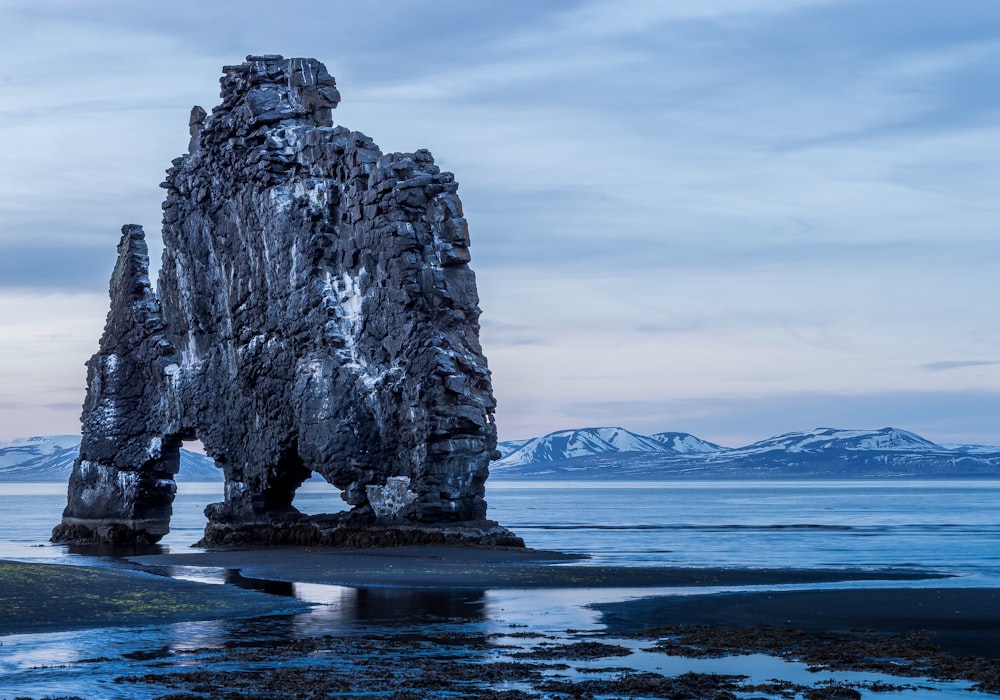 black rock formation on seashore under cloudy sky at daytime