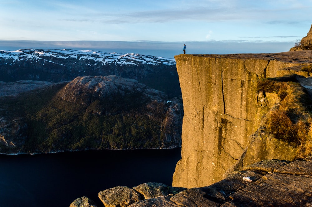 silhouette photo of person standing on cliff under cloudy sky during daytime