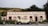 A vintage car is parked in front of a rustic building labeled 'Cardrona Hotel'. The building has a classic facade with cream-colored walls and red accents. It is surrounded by green shrubs and there is a mountainous landscape in the background, with greenery covering the hills.