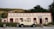 A vintage car is parked in front of a rustic building labeled 'Cardrona Hotel'. The building has a classic facade with cream-colored walls and red accents. It is surrounded by green shrubs and there is a mountainous landscape in the background, with greenery covering the hills.