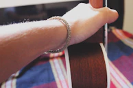 Close-up of hands strumming an acoustic guitar surrounded by colorful festival wristbands.