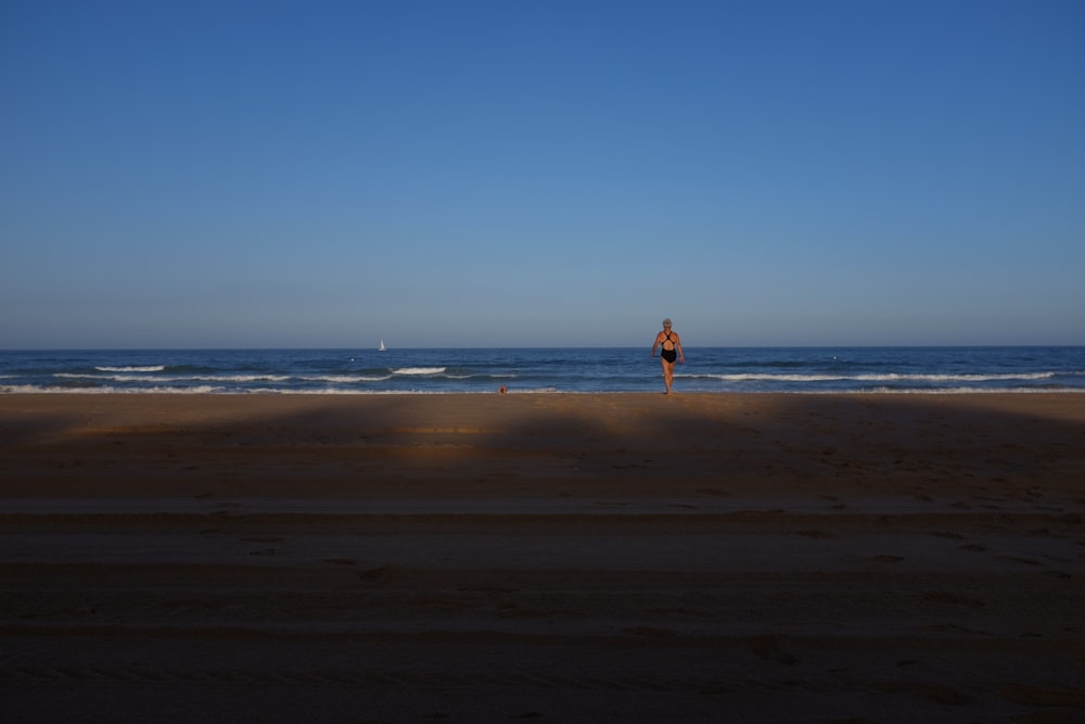 woman in black one-piece swimsuit facing blue wavy ocean under clear blue sky