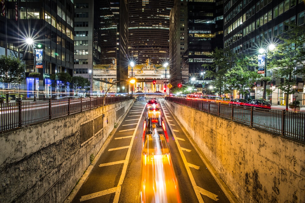 Zeitrafferfotografie eines Fahrzeugs, das nachts auf einer Betonstraße vorbeifährt, die Hochhäuser umgibt