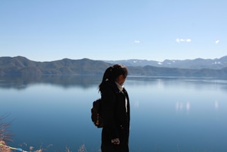 A backpacker setting up camp beside a serene alpine lake under a clear blue sky.