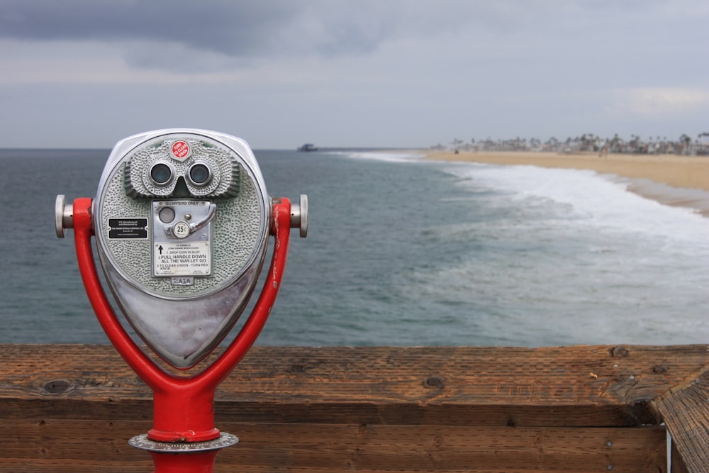 grey and red coin operated binoculars in front of seawaves under nimbus clouds during daytime