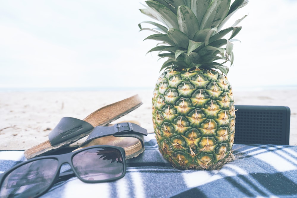 green and yellow pineapple besides black slide slippers and sunglasses