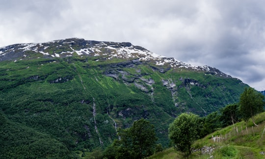green plant covered mountain with ice caps under cloudy skies in Geiranger Norway