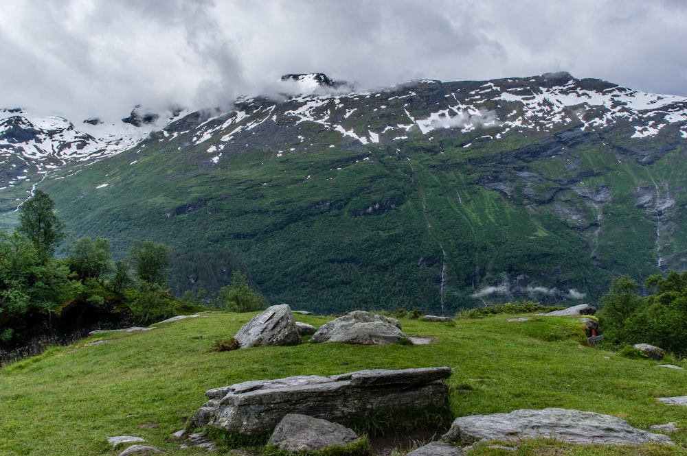 rochas cinzas e pretas cercadas por grama verde perto da montanha sob o céu branco durante o dia