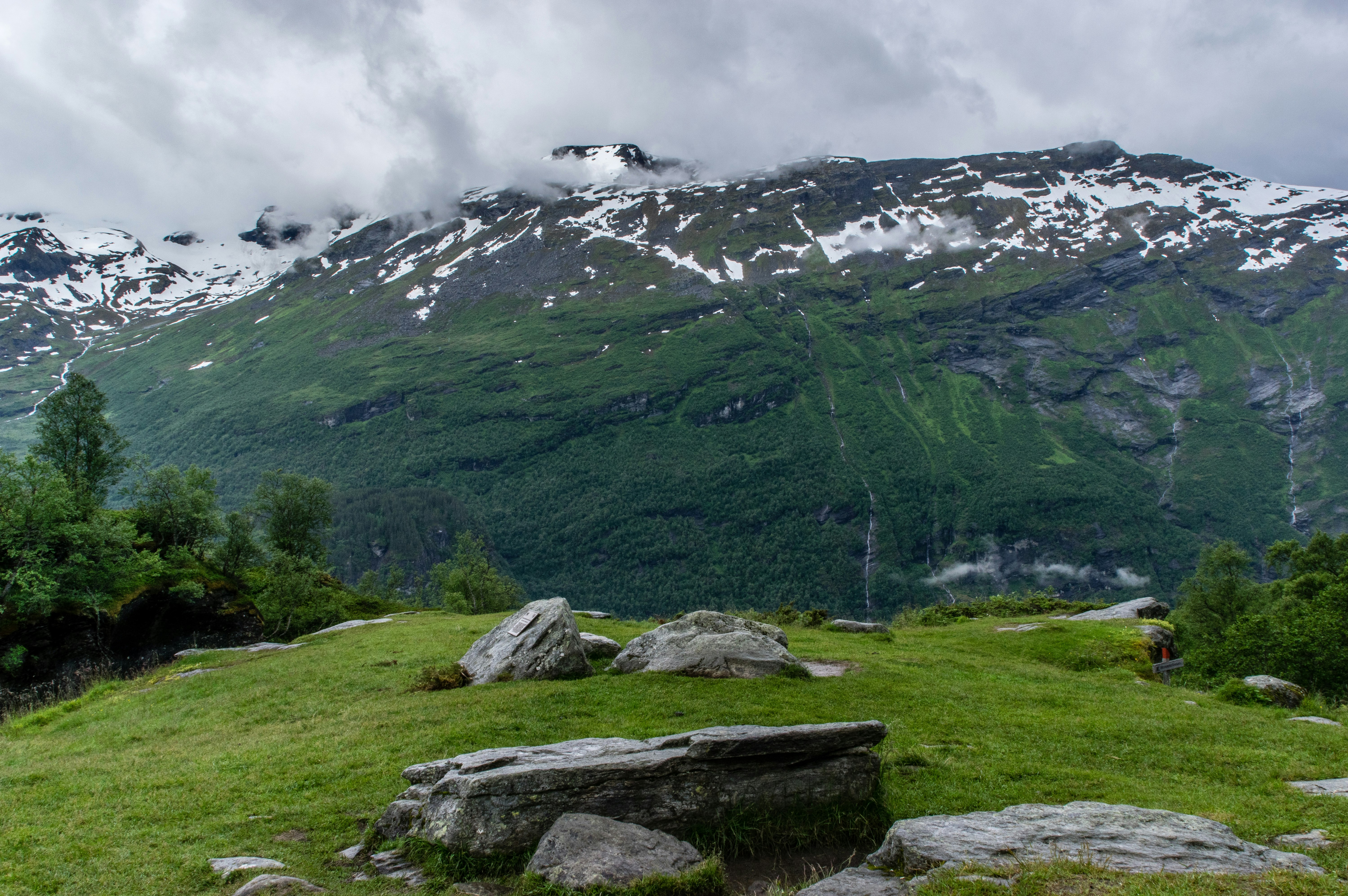 gray and black rocks surrounded by green grass near mountain under white sky at daytime