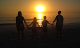 A warm family circle holding hands on a sandy beach at sunset, embodying connection and calm leadership.