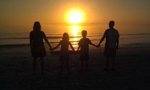 A warm family circle holding hands on a sandy beach at sunset, embodying connection and calm leadership.