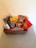 A wicker basket filled with various packaged candies and chocolates, including brands like Starburst, Kinder, and Allen's. The basket is placed on a light-colored surface with a plain background.