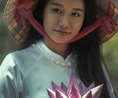 woman wearing white long-sleeved dress and brown sungat holding pink petaled flower