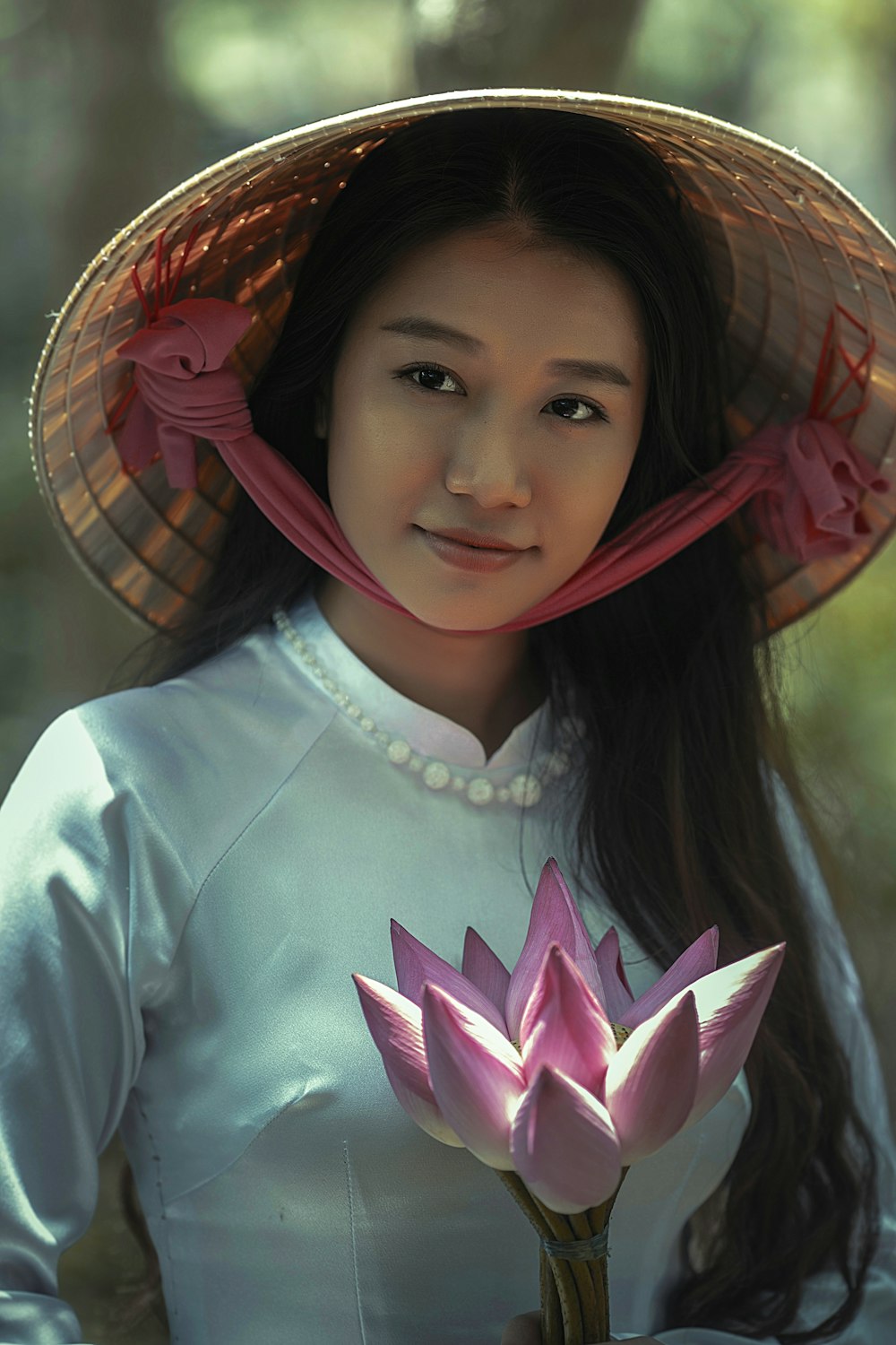 woman wearing white long-sleeved dress and brown sungat holding pink petaled flower