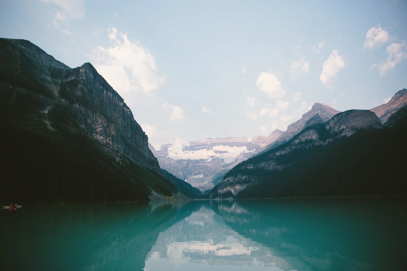 Lake Louise, Banff National Park — the flat grey lake surface reflects the surrounding mountains and evergreen forest