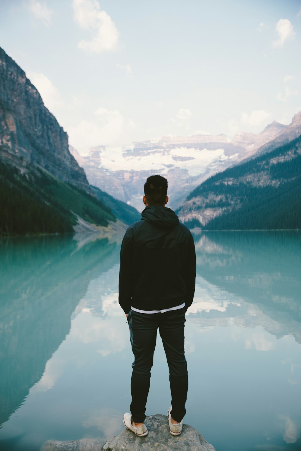 Mann steht in der Mitte des Felsens mit Blick auf den See