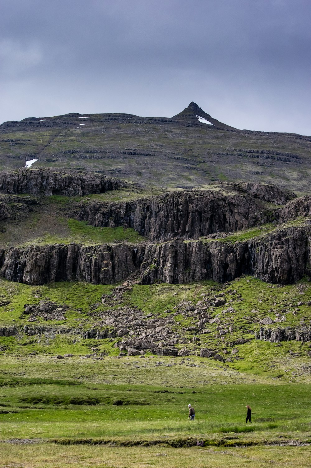 two person walking on green grass field with mountain