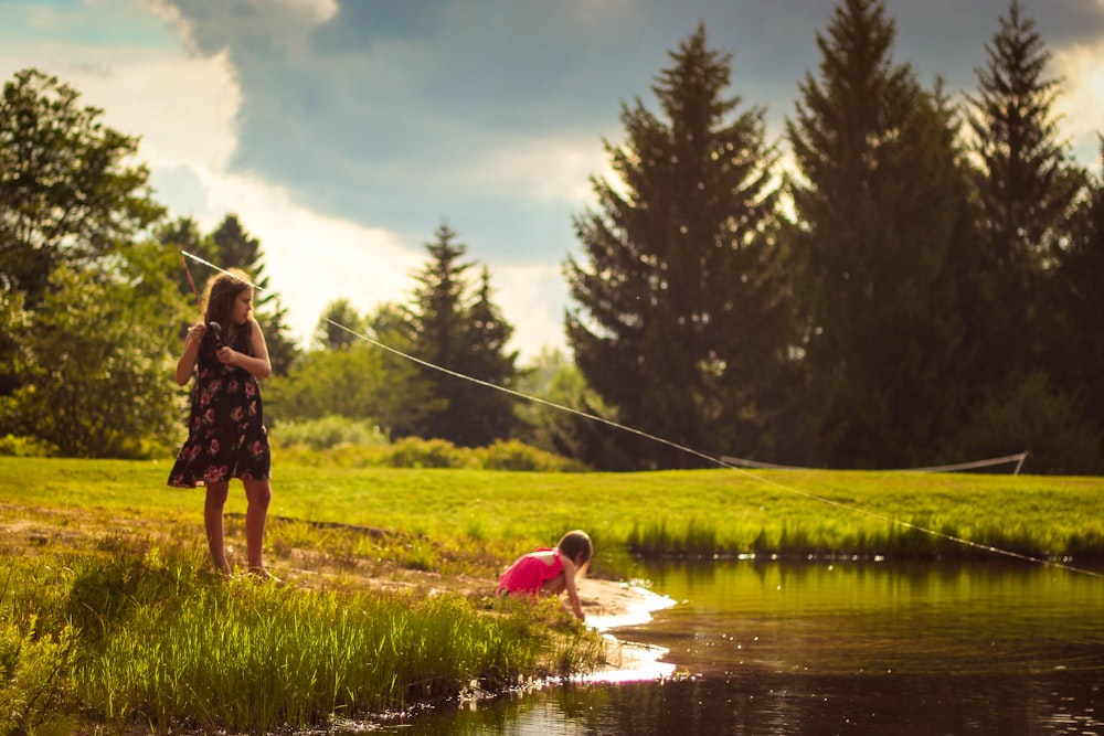 girl standing green grass field beside lake during daytime