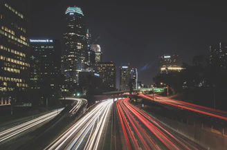 A vibrant city skyline glowing under a dark sky, with streaks of car lights weaving through streets.