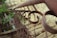 A rustic metal railing features a series of circular designs, extending into the distance with a slightly blurred background. The railing is weathered, with hints of rust, and it contrasts against the surrounding greenery and stone textures.