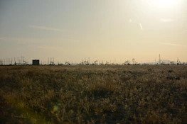 Wide shot of a rugged landscape dotted with oil extraction equipment under a clear sky.