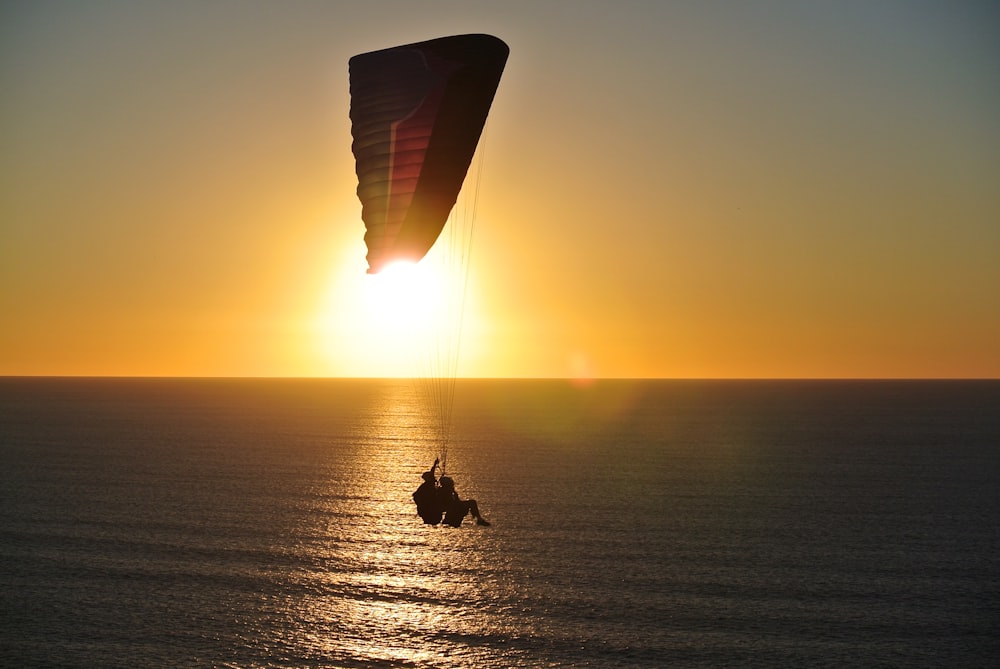 person in parachute above body of water during golden hour