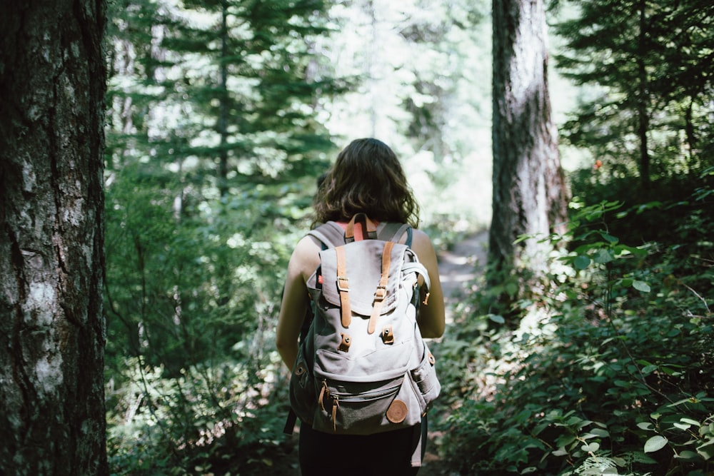 femme en haut sans manches et sac à dos entouré d’arbres pendant la journée