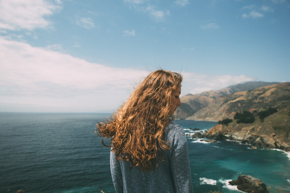 woman standing facing the ocean during daytime