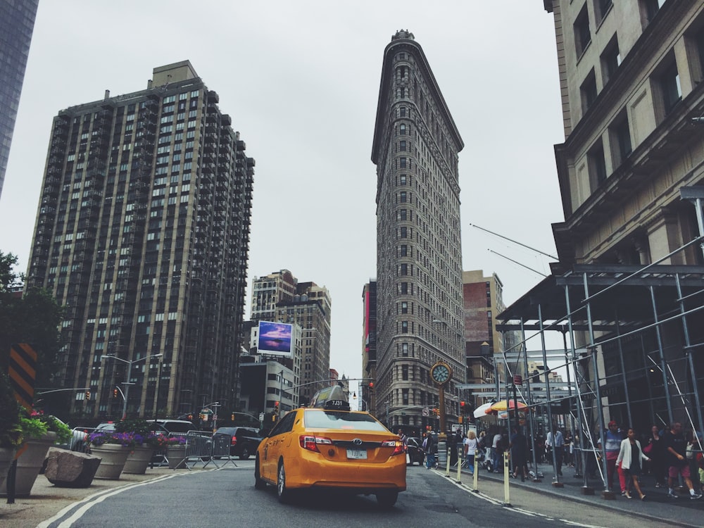 yellow taxicab passing by buildings during daytime