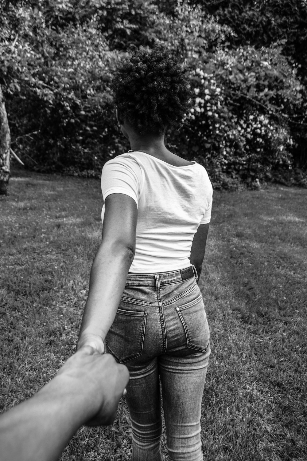 greyscale photography of woman walking with hand at the back holding other hand