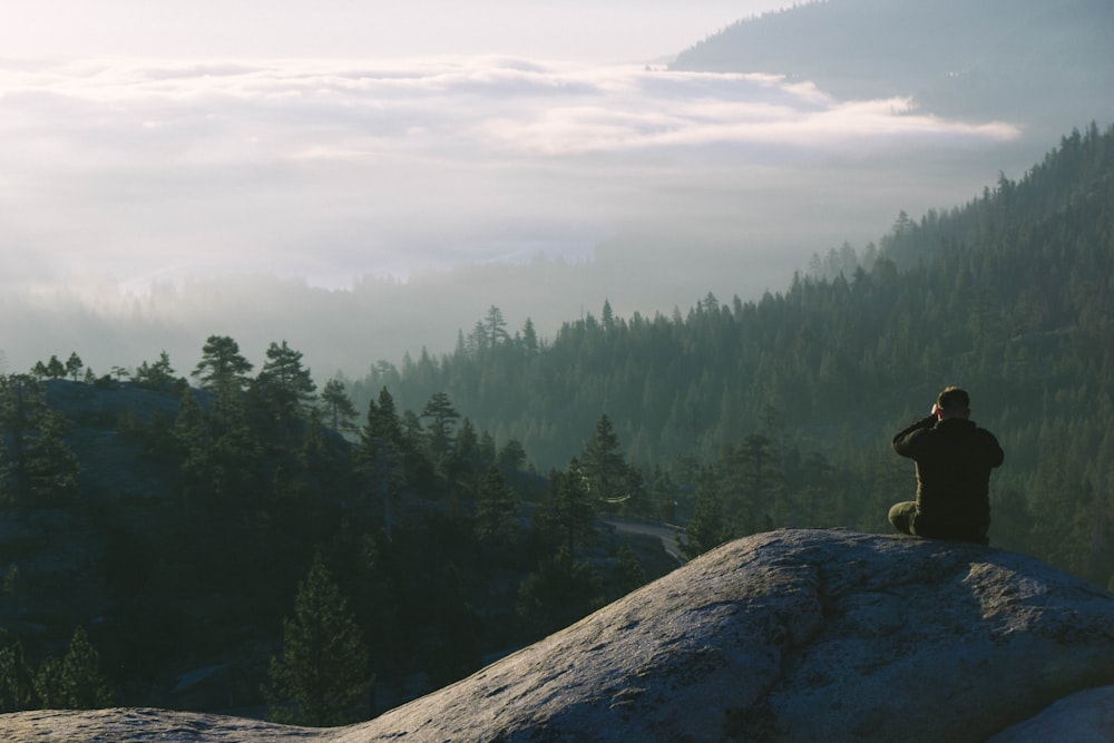 man sits on the mountain facing landscape view