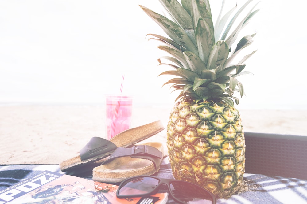 Minimalistische Fotografie von Ananas in der Nähe von Sandalen und Sonnenbrillen