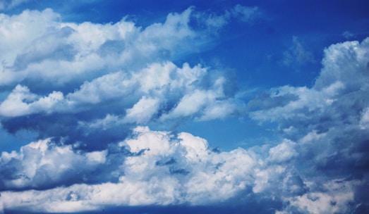 Dynamic and textured clouds are set against a vibrant blue sky, showcasing a variety of cloud formations and white fluffy textures.