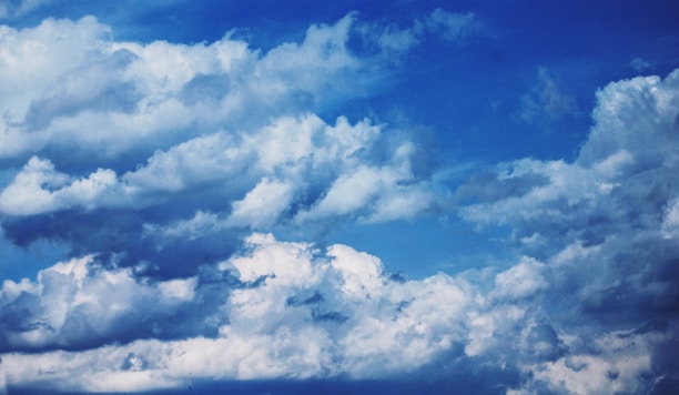 Dynamic and textured clouds are set against a vibrant blue sky, showcasing a variety of cloud formations and white fluffy textures.