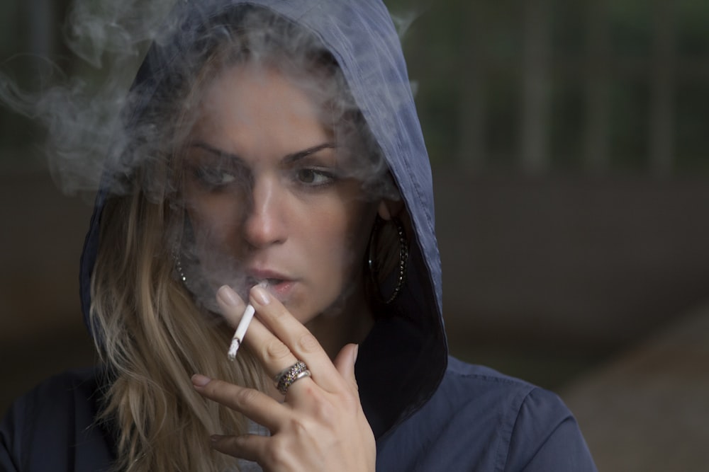 mujer con sudadera con capucha mientras sostiene un cigarrillo