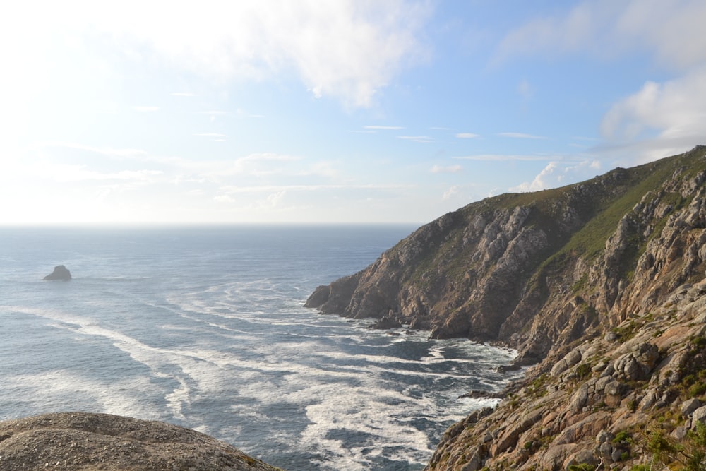 sea hitting seashore beside brown rock mountains under blue sky