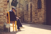 Portrait of an elderly Italian man sitting outside a rustic café, deep in thought.
