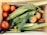 A wooden crate filled with fresh produce, including several ripe red tomatoes, ears of corn with husks, and a few peaches. Nestled among the vegetables is a small pepper. The arrangement showcases a variety of textures and natural colors.